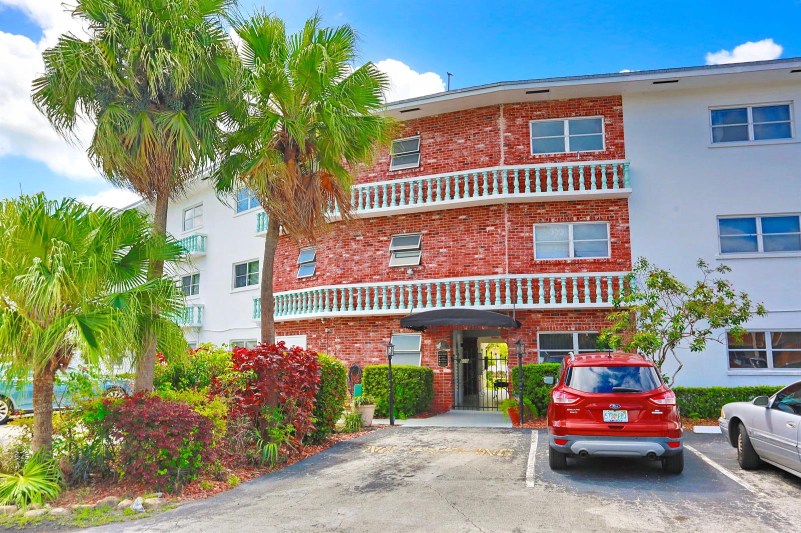 A three-story brick apartment building features balconies, a central entrance, and a parking lot — 600 Pine Drive # 209, Pompano Beach FL 33060, POMPANO BEACH, FL
