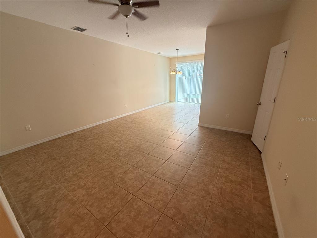 An empty room with beige tile flooring, a ceiling fan, and sliding glass patio doors — 9460 STRONGBARK LANE, ORLANDO, FL