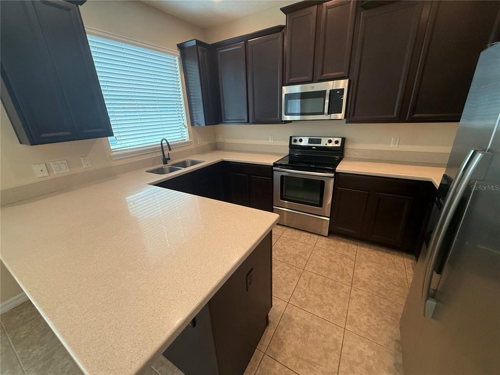 A kitchen features dark wood cabinets, light countertops, stainless steel appliances, and tile flooring — 9460 STRONGBARK LANE, ORLANDO, FL