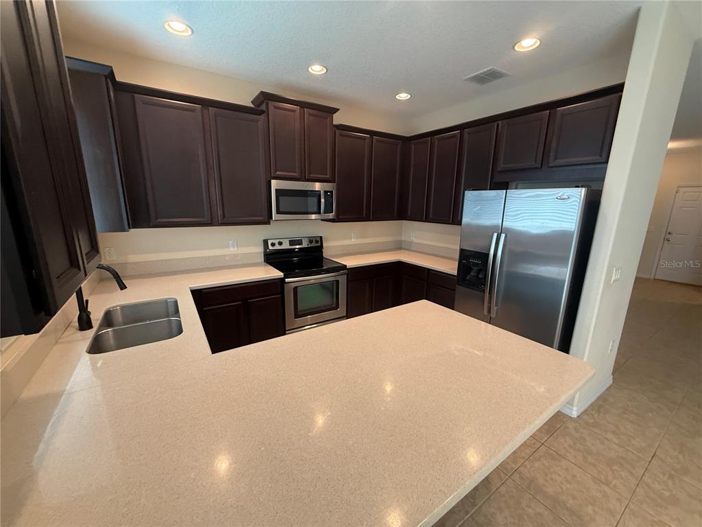 A kitchen with dark wood cabinets, stainless steel appliances, and light-colored countertops — 9460 STRONGBARK LANE, ORLANDO, FL