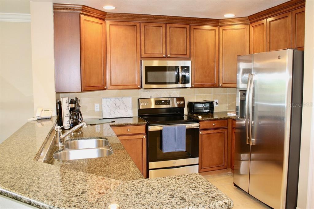 A kitchen features wood cabinets, granite countertops, stainless steel appliances, and a double sink — 7604 CABANA CT UNIT 303, REUNION, FL