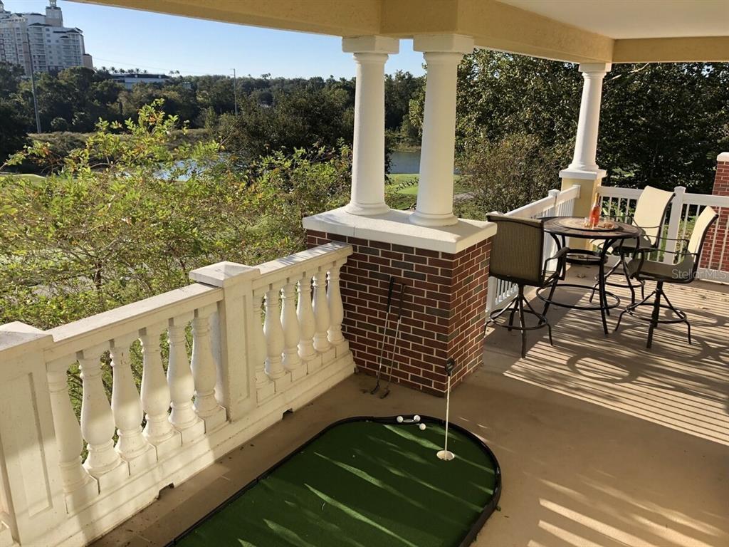 A covered balcony features a putting green, a small bistro table, and views of trees — 7604 CABANA CT UNIT 303, REUNION, FL