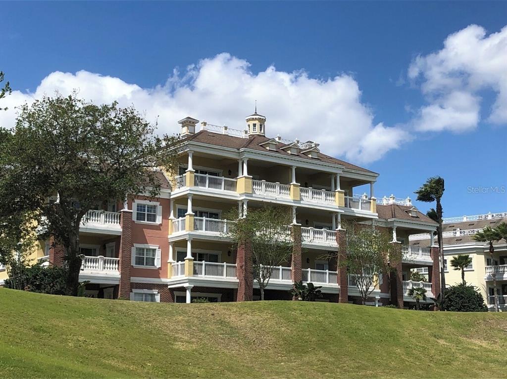 A multi-story residential building with balconies and a cupola sits above a grassy hill — 7604 CABANA CT UNIT 303, REUNION, FL