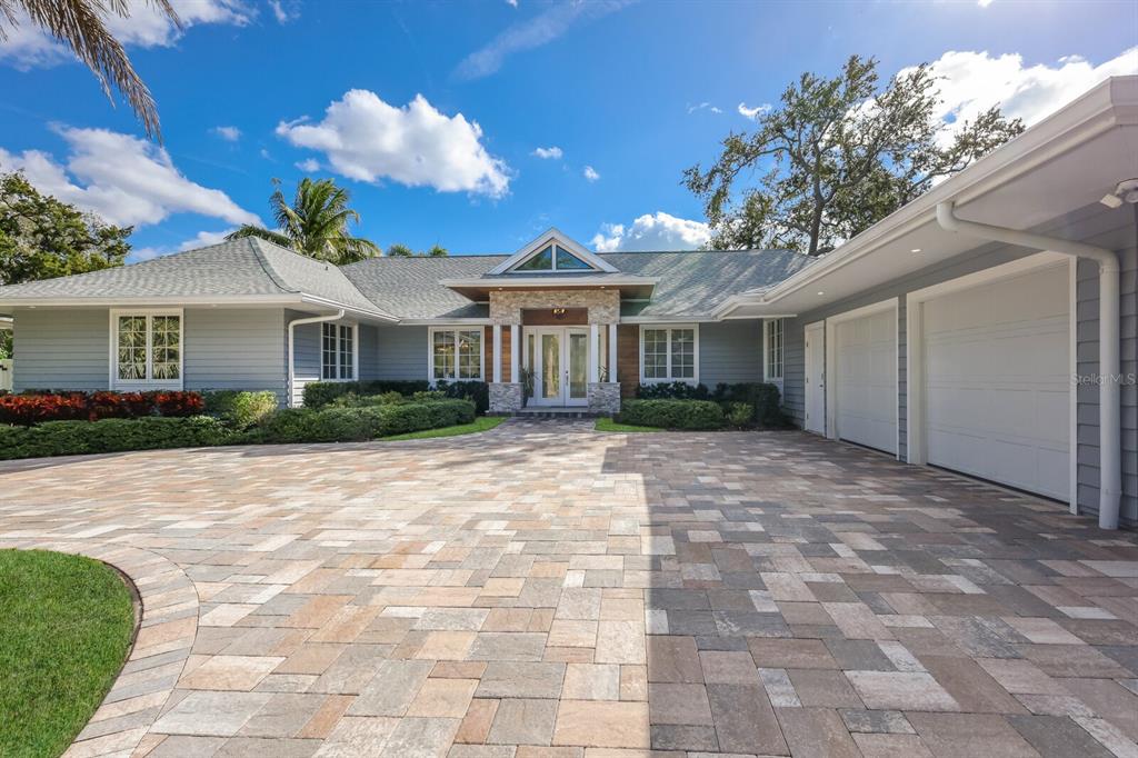 A single-story house with a stone-accented entryway, gray siding, and a large paver driveway — 1253 N BASIN LANE, SARASOTA, FL