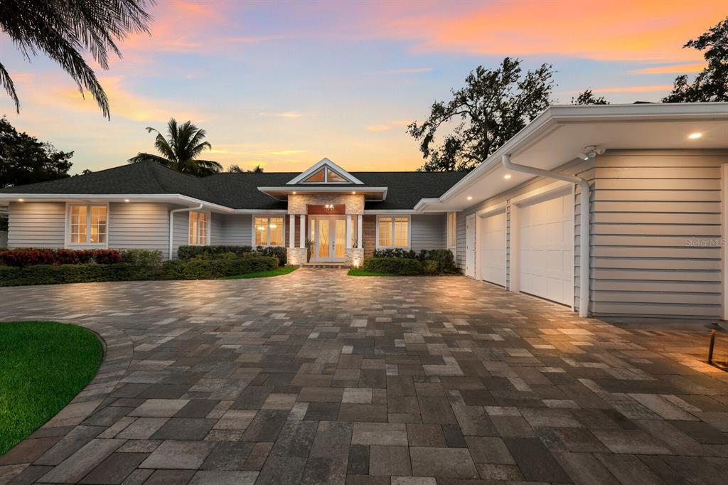 A single-story house with a paved driveway, three-car garage, and a stone-accented entryway at sunset — 1253 N BASIN LANE, SARASOTA, FL