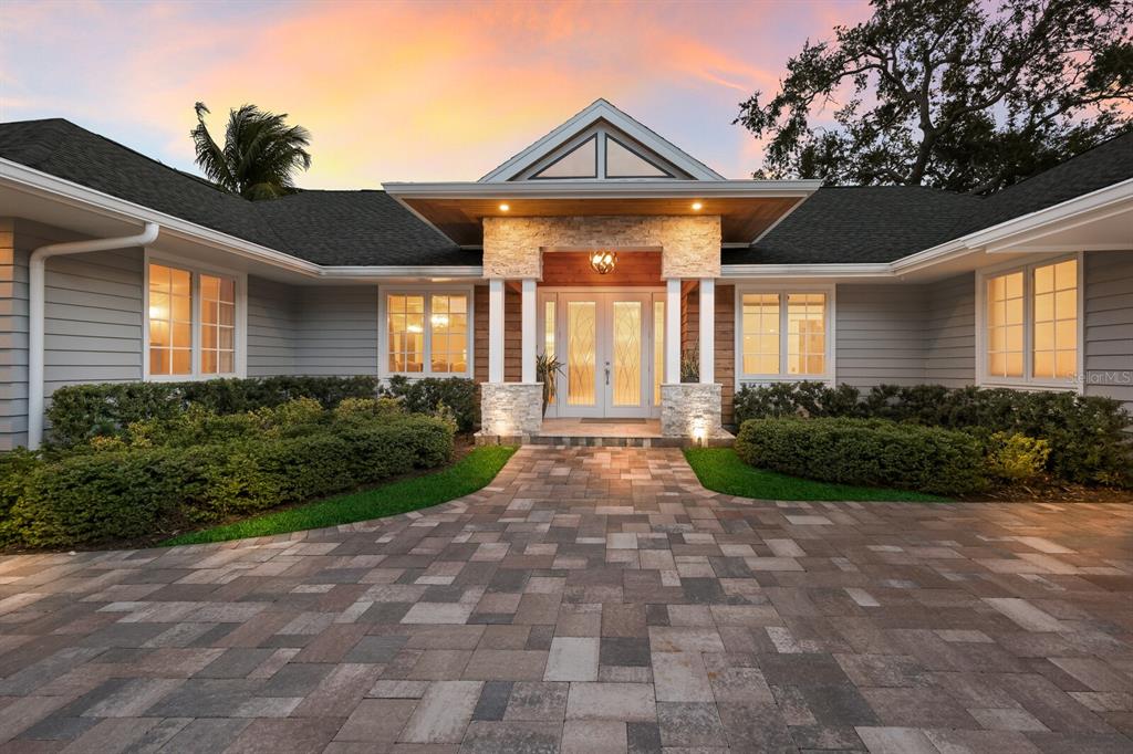 A single-story house with a stone-pillared entryway, gray siding, and a paved driveway at sunset — 1253 N BASIN LANE, SARASOTA, FL