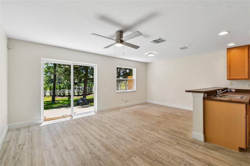 An open-concept room features light wood-look tile flooring, a ceiling fan, and sliding glass doors — 4084 PITCH PINE CIRCLE, OVIEDO, FL