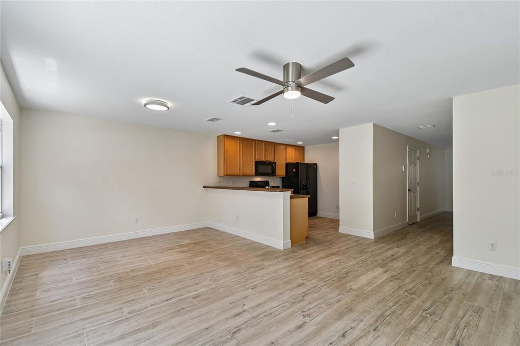 An open-concept living area features light wood-look tile flooring, a ceiling fan, and a kitchen — 4084 PITCH PINE CIRCLE, OVIEDO, FL