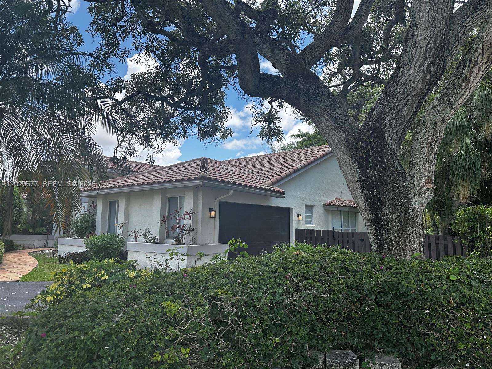 A single-story house with a tile roof and a dark garage door sits behind landscaping — 1200 NW 101st Ave, Plantation FL 33322, PLANTATION, FL