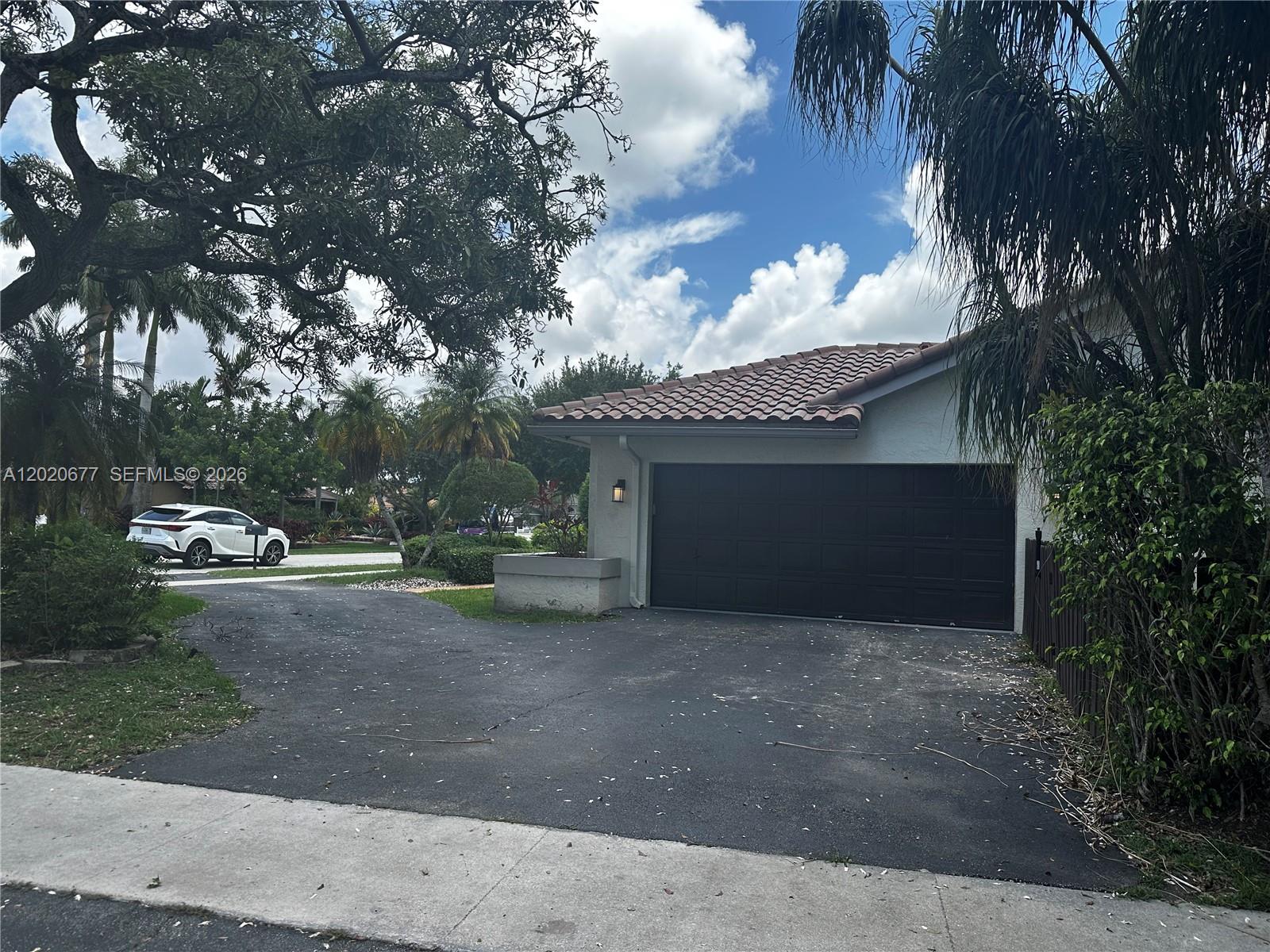 A dark garage door is attached to a house with a tiled roof and driveway — 1200 NW 101st Ave, Plantation FL 33322, PLANTATION, FL