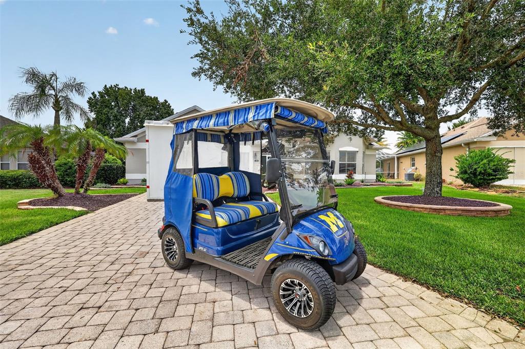 A blue and yellow golf cart sits on a paved driveway in front of a house — 1218 CAMERO DRIVE, LADY LAKE, FL