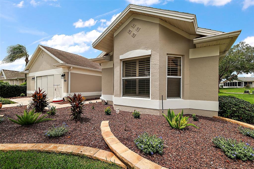 A tan single-story house with a garage, brown rock landscaping, and a stone-edged garden bed — 1218 CAMERO DRIVE, LADY LAKE, FL