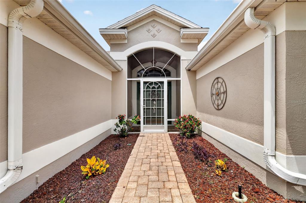 A paved walkway leads to the front entrance of a house with beige stucco walls — 1218 CAMERO DRIVE, LADY LAKE, FL