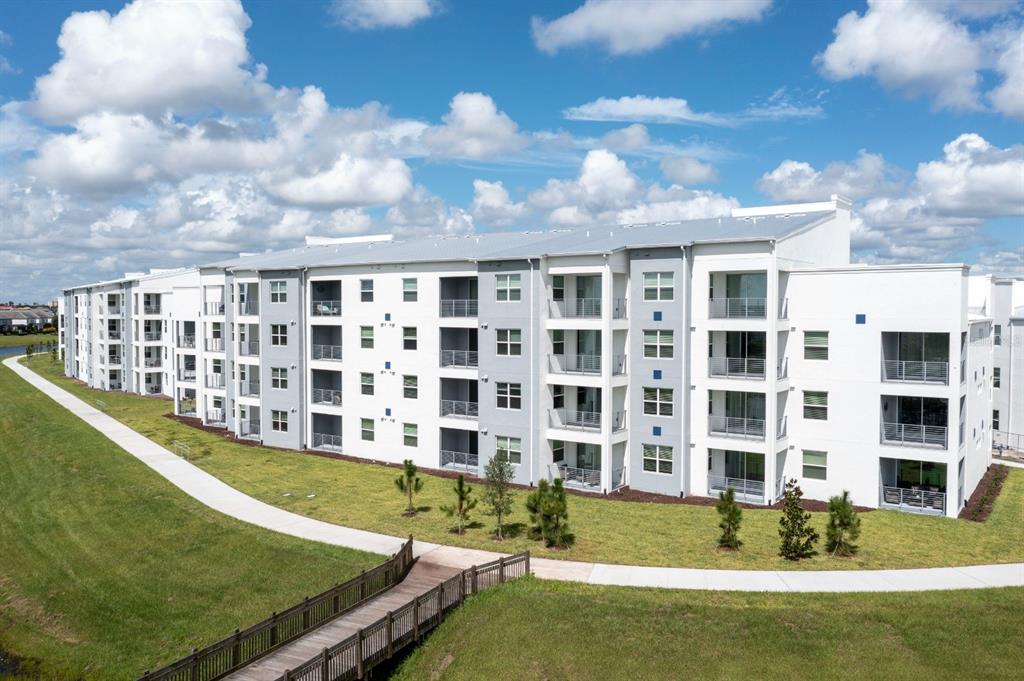 An exterior view of a multi-story apartment building with balconies and a wooden footbridge — 3161 PARADOX CIRCLE UNIT 304, KISSIMMEE, FL