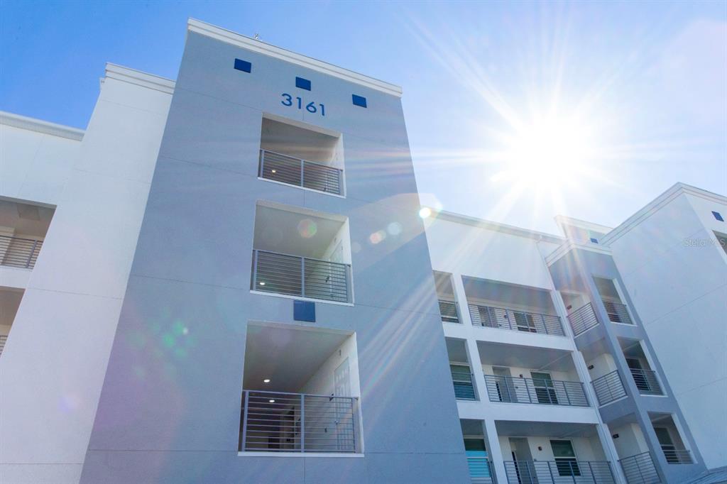 A low-angle exterior view of a modern multi-story apartment building with blue and white siding — 3161 PARADOX CIRCLE UNIT 304, KISSIMMEE, FL
