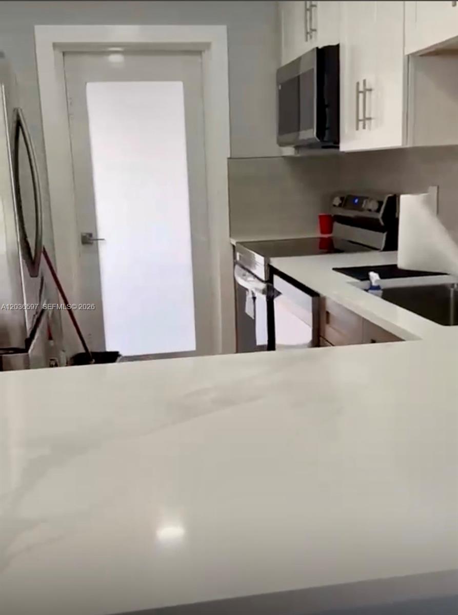 A kitchen features white cabinets, stainless steel appliances, and a white countertop peninsula — 2940 N Course Dr # 311, Pompano Beach FL 33069, POMPANO BEACH, FL