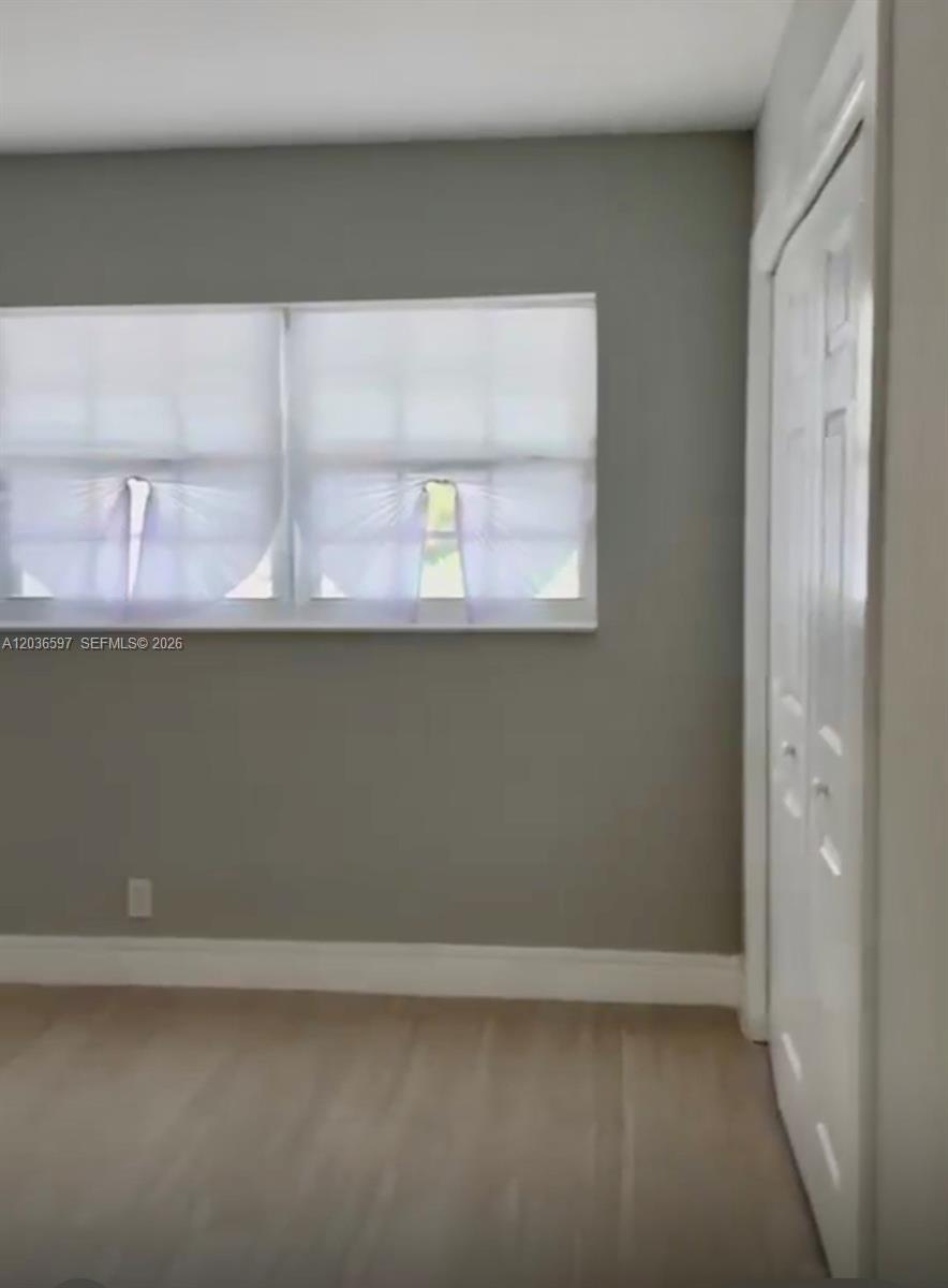 A room with gray walls, light wood-look flooring, a window with white shades, and a closet — 2940 N Course Dr # 311, Pompano Beach FL 33069, POMPANO BEACH, FL