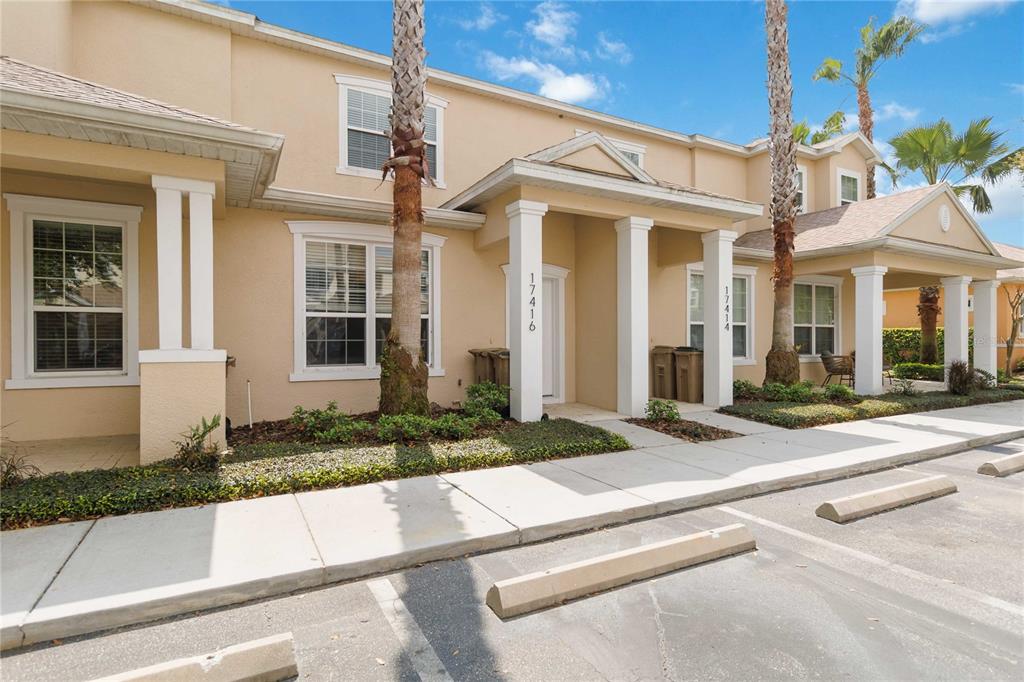 A beige two-story townhouse exterior features white columns, a sidewalk, and a parking lot — 17416 PLACIDITY AVENUE, CLERMONT, FL