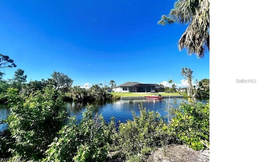 A house with a screened lanai sits across a canal surrounded by lush vegetation — 2703 CEITUS PARKWAY, CAPE CORAL, FL