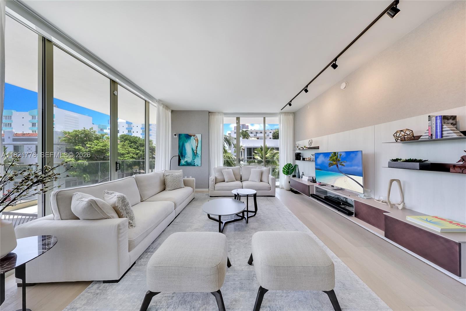 A modern living room features white sofas, two ottomans, a television, and floor-to-ceiling windows — 300 Collins Ave # 3D, Miami Beach FL 33139, MIAMI BEACH, FL