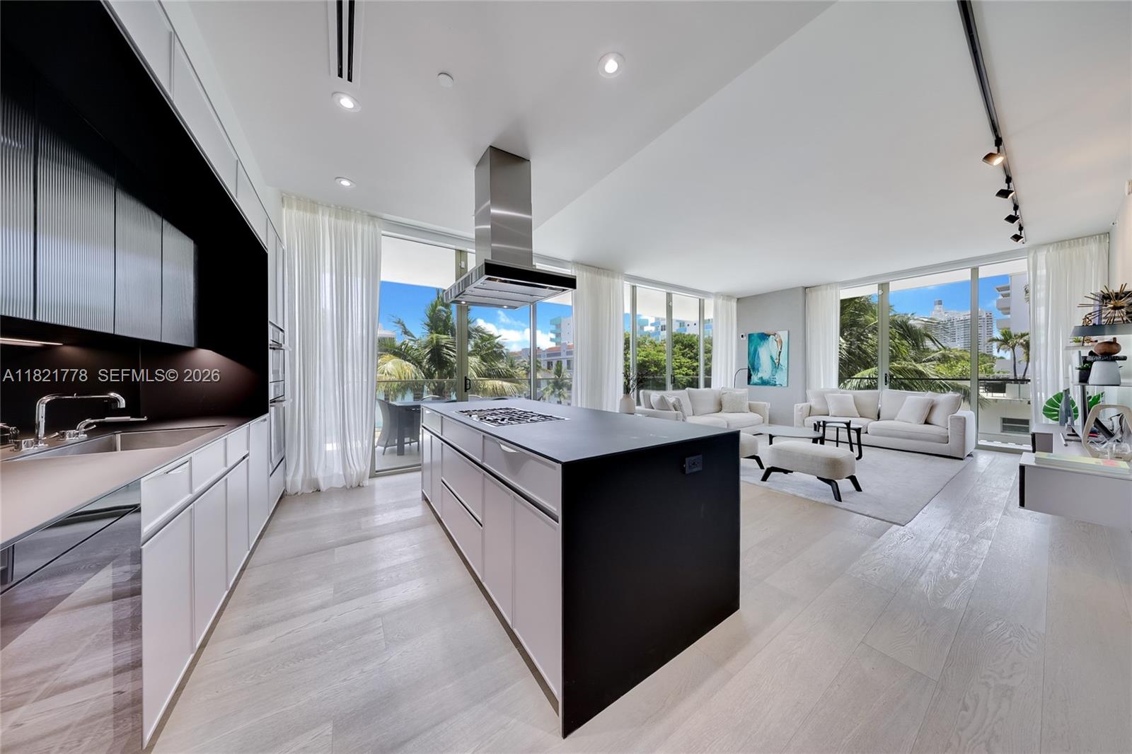 A modern kitchen with a black island and white cabinets opens to a bright living area — 300 Collins Ave # 3D, Miami Beach FL 33139, MIAMI BEACH, FL