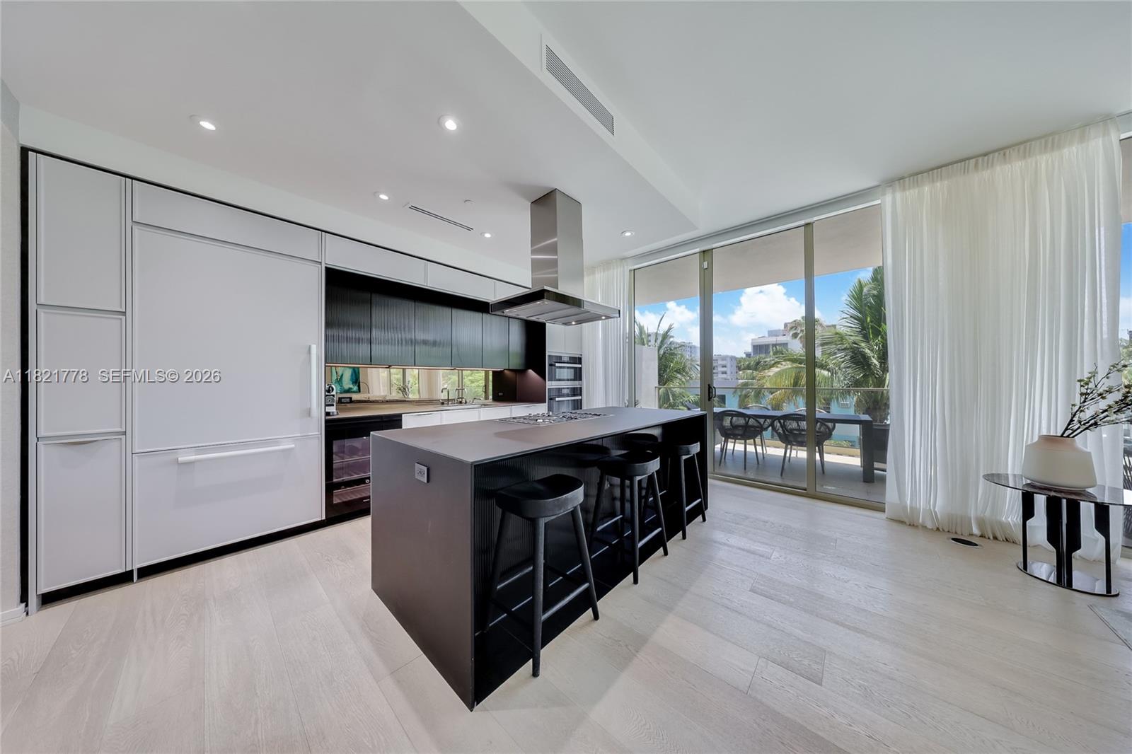 A modern kitchen features a dark island with bar stools, white cabinetry, and floor-to-ceiling windows — 300 Collins Ave # 3D, Miami Beach FL 33139, MIAMI BEACH, FL