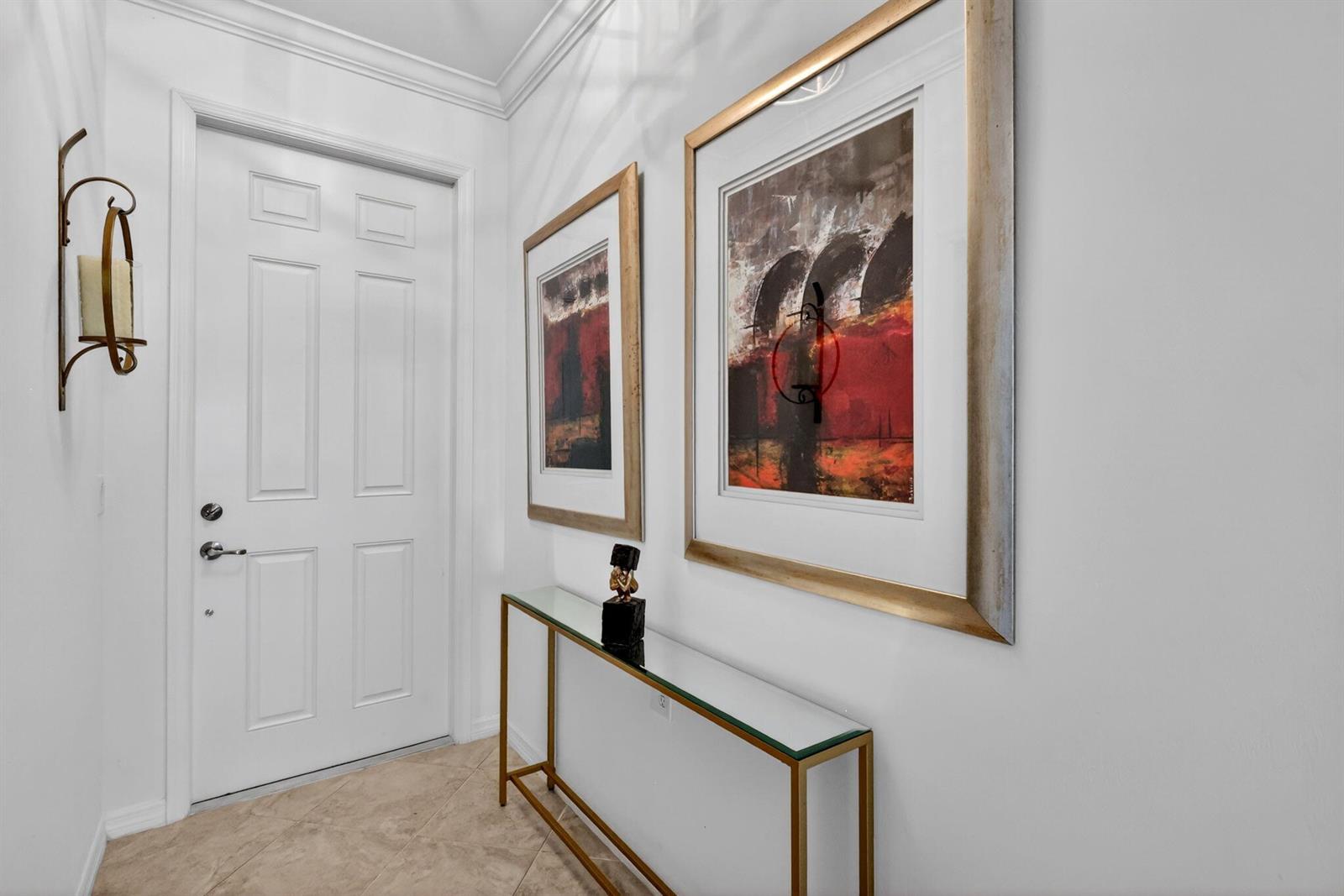 A hallway features a white door, a glass console table, and two framed abstract paintings — 43050 Greenway Boulevard # 645, Punta Gorda FL 33982, PUNTA GORDA, FL