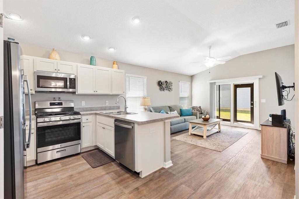 An open-concept kitchen and living area features white cabinets, stainless steel appliances, and wood flooring — 3948 MUNFORD TERRACE, THE VILLAGES, FL