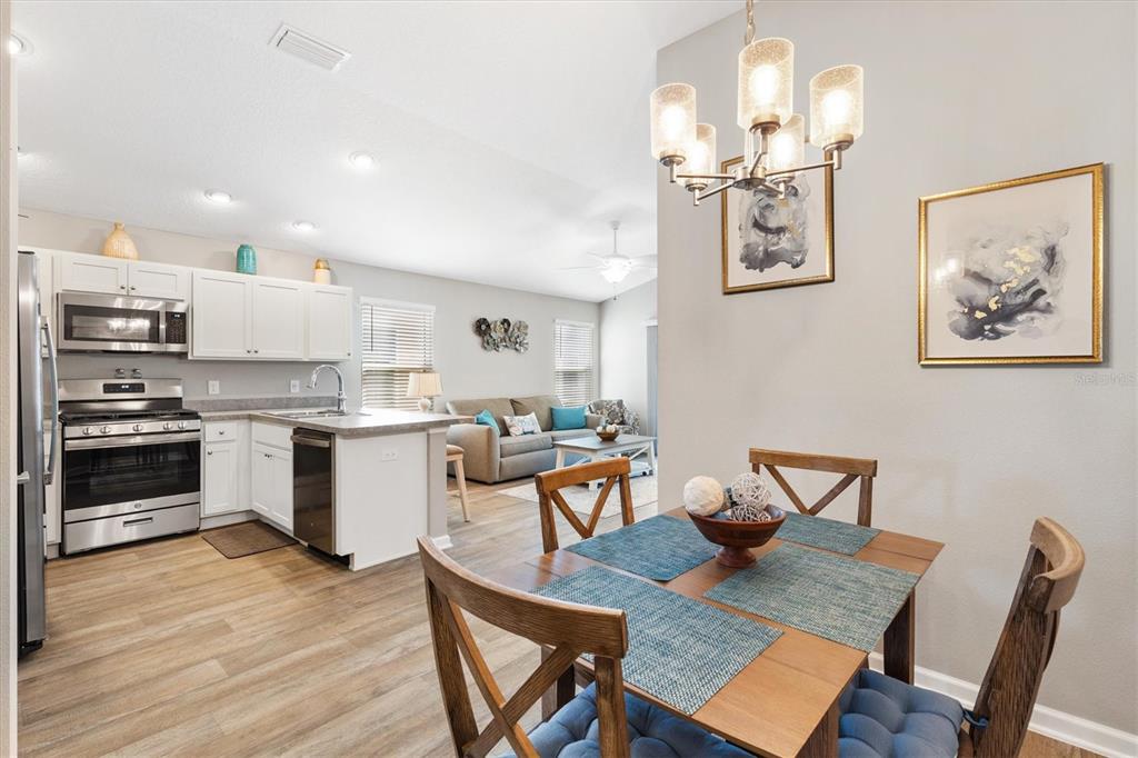 An open-concept kitchen and dining area with white cabinets, stainless appliances, and wood-look flooring — 3948 MUNFORD TERRACE, THE VILLAGES, FL