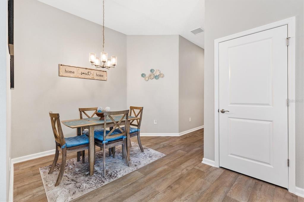A dining area features a wooden table with four chairs, a chandelier, and wood-look flooring — 3948 MUNFORD TERRACE, THE VILLAGES, FL