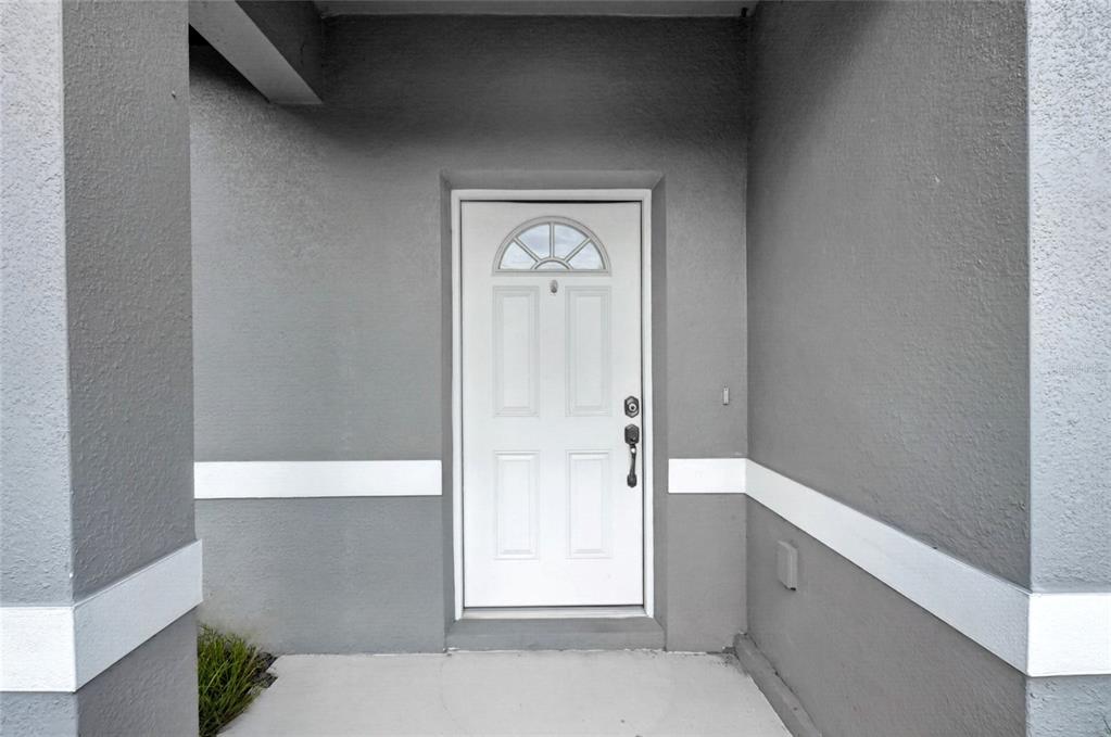 A white front door with a small arched window is set into a gray exterior wall — 1400 SEBRING WAY, POINCIANA, FL