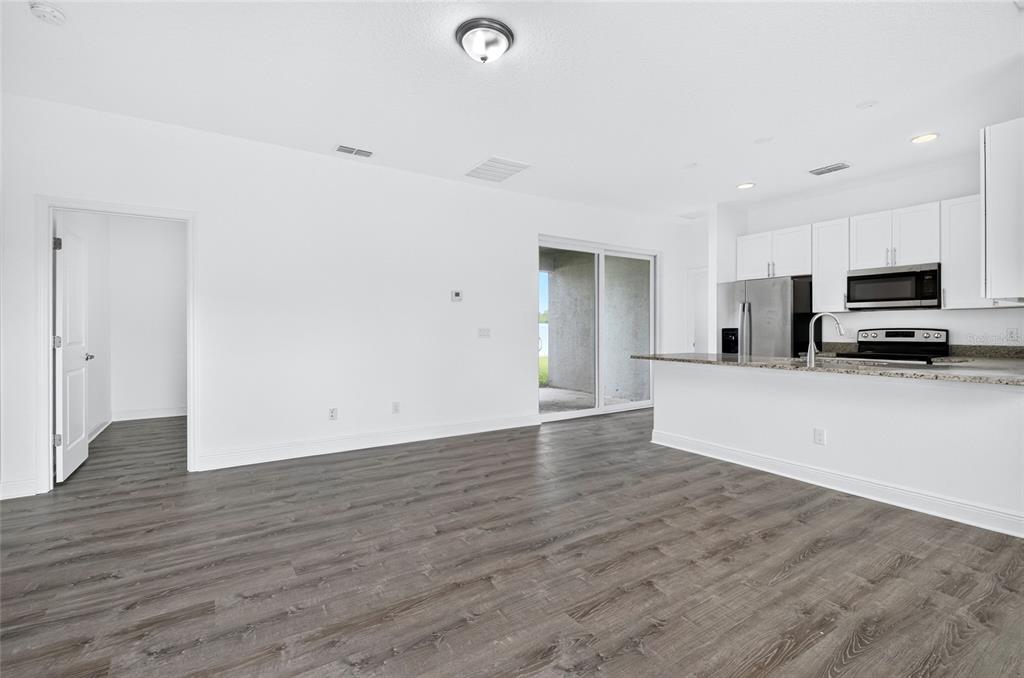 An open-concept living area features wood-look flooring, white walls, and a kitchen with white cabinets — 1400 SEBRING WAY, POINCIANA, FL