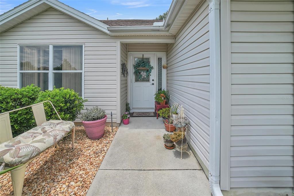 A beige-sided house exterior features a concrete walkway leading to a white front door — 8371 SE 168TH TRINITY PLACE, THE VILLAGES, FL