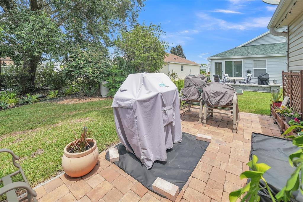 A backyard patio features a covered grill, outdoor furniture, and a grassy lawn — 8371 SE 168TH TRINITY PLACE, THE VILLAGES, FL