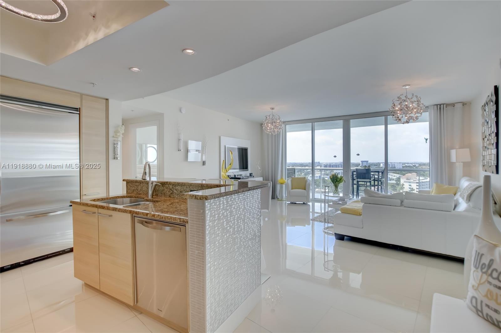 A modern kitchen with light wood cabinets and granite countertops overlooks a bright living area — 1 N Ocean Blvd # 1011, Pompano Beach FL 33062, POMPANO BEACH, FL