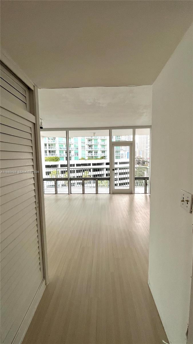An empty room with light wood-look flooring features floor-to-ceiling windows and a balcony door — 1408 Brickell Bay Dr # 916, Miami FL 33131, MIAMI, FL