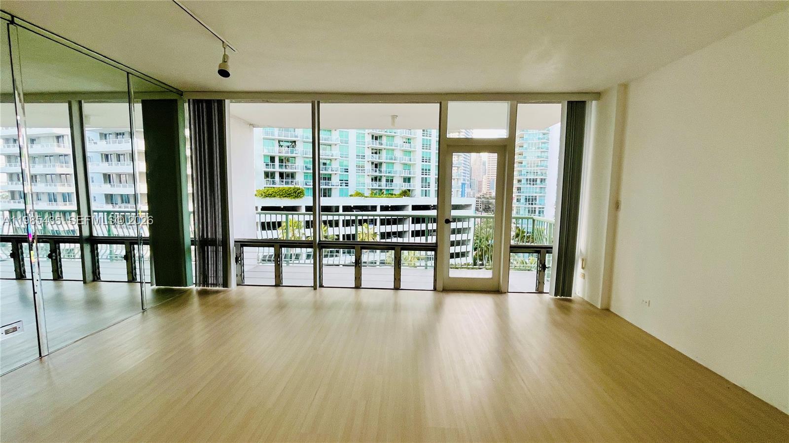 An empty room with light wood flooring, floor-to-ceiling windows, and a balcony overlooking city buildings — 1408 Brickell Bay Dr # 916, Miami FL 33131, MIAMI, FL