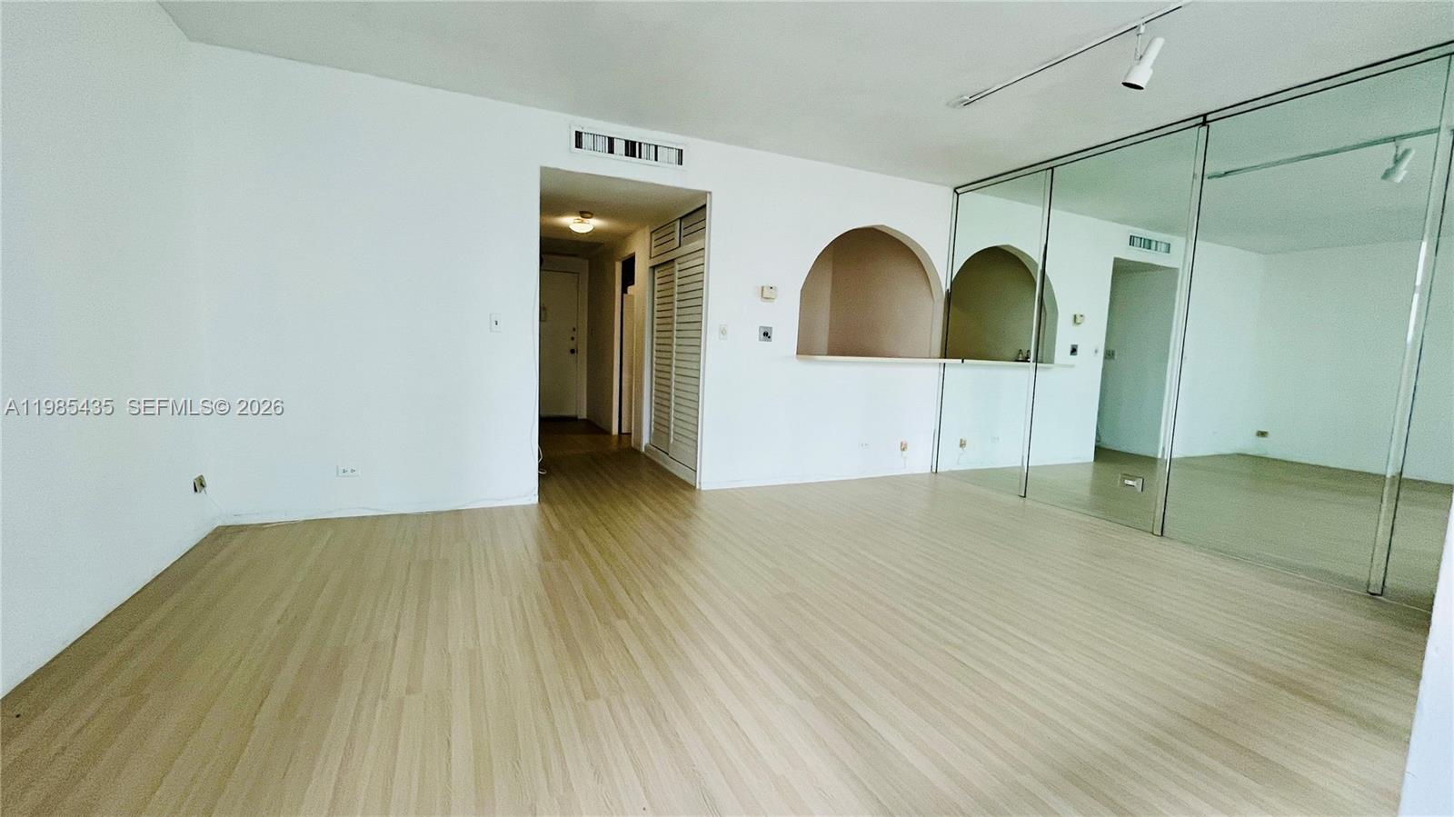 An empty room features light wood-look flooring, white walls, and a large mirrored wall — 1408 Brickell Bay Dr # 916, Miami FL 33131, MIAMI, FL
