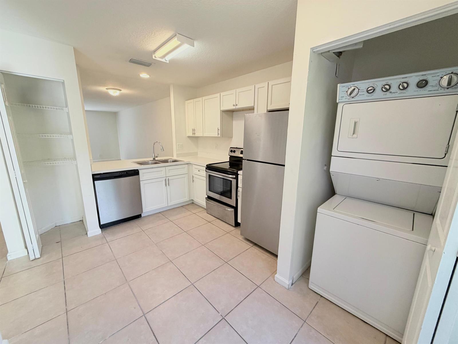 A kitchen features white cabinets, stainless steel appliances, tile flooring, and an adjacent laundry closet — 910 Summit Lake Drive, West Palm Beach FL 33406, WEST PALM BEACH, FL