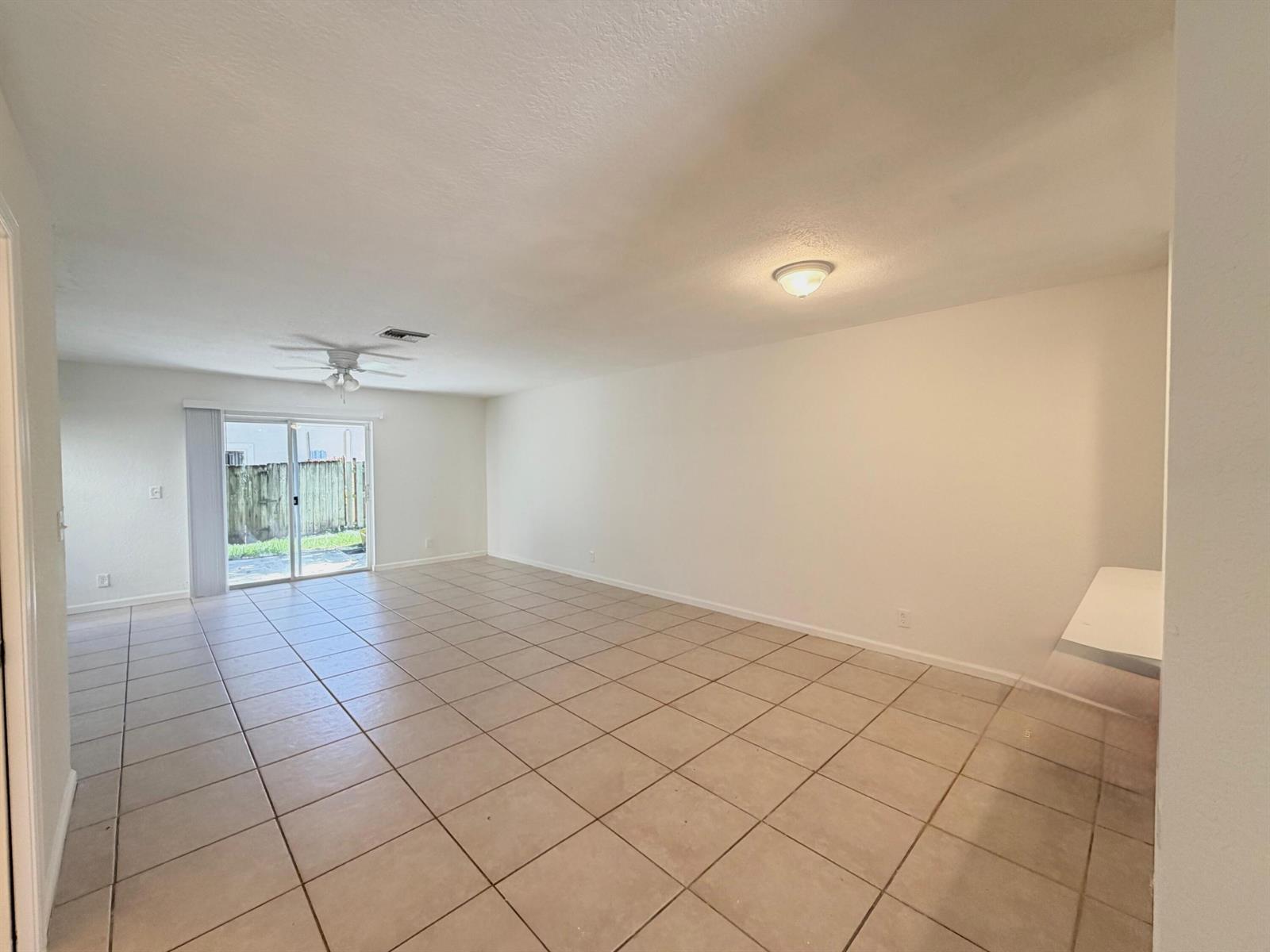An empty living room features beige tile flooring, white walls, a ceiling fan, and sliding doors — 910 Summit Lake Drive, West Palm Beach FL 33406, WEST PALM BEACH, FL