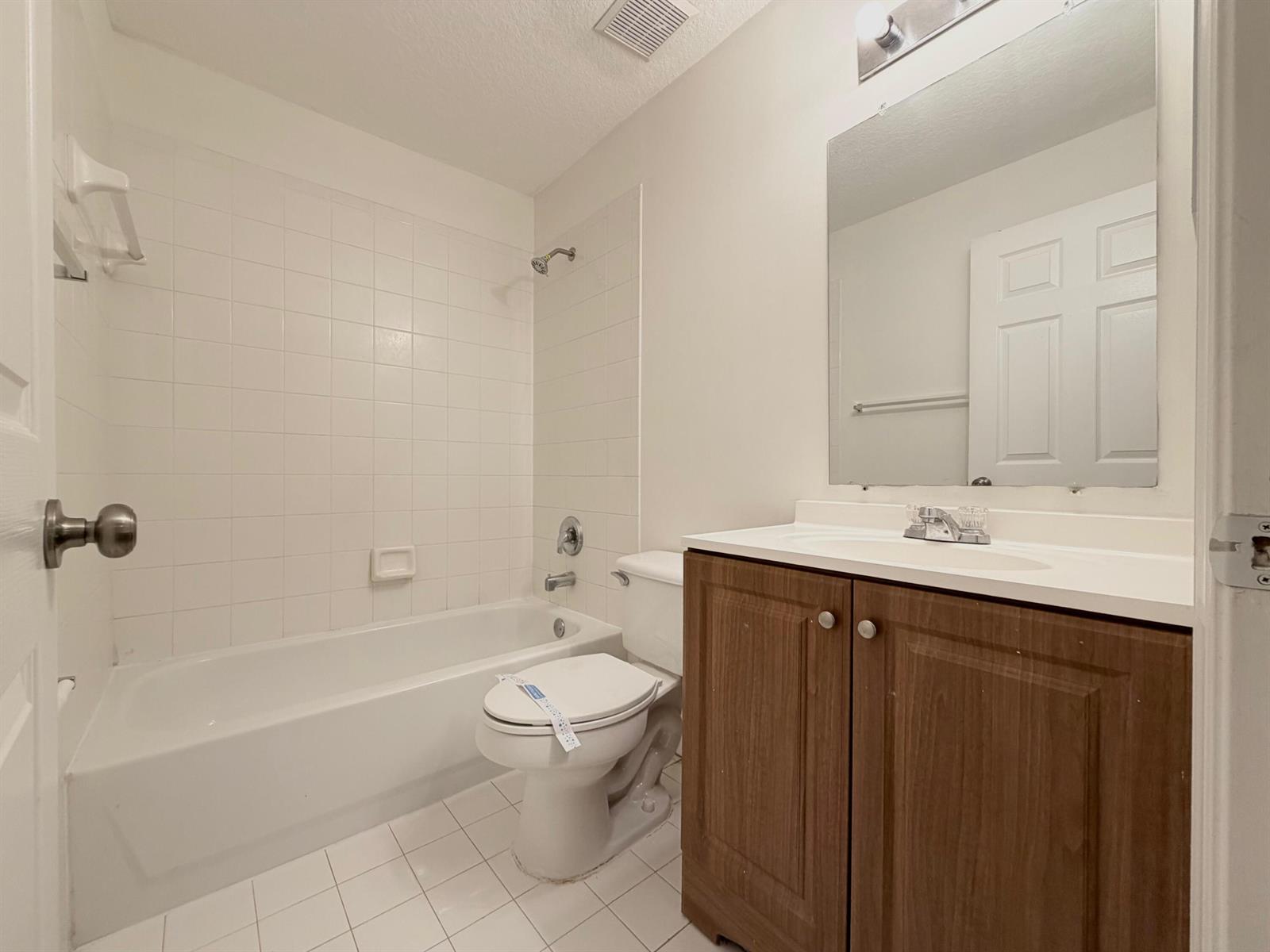 A bathroom features a white tub-shower combo, a toilet, and a wood-toned vanity with mirror — 910 Summit Lake Drive, West Palm Beach FL 33406, WEST PALM BEACH, FL