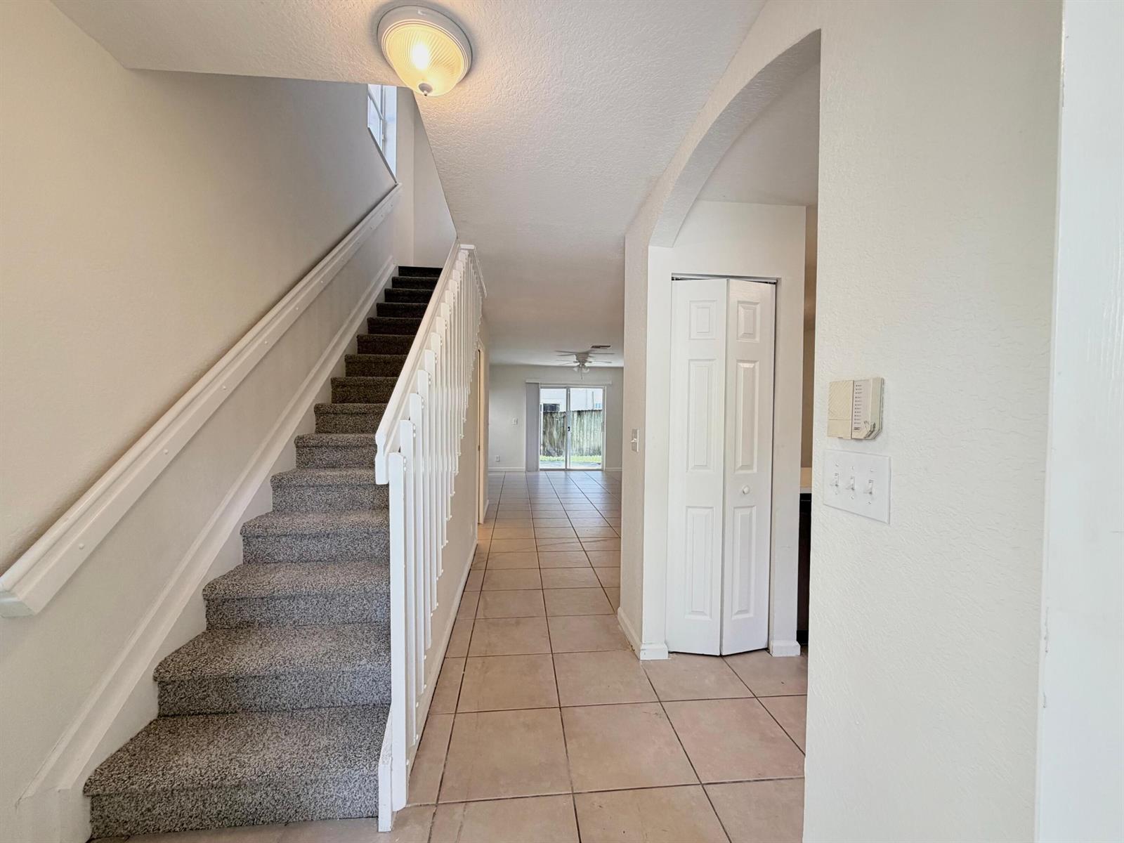 An entryway features a carpeted staircase with white railings, tile flooring, and a hallway leading back — 910 Summit Lake Drive, West Palm Beach FL 33406, WEST PALM BEACH, FL