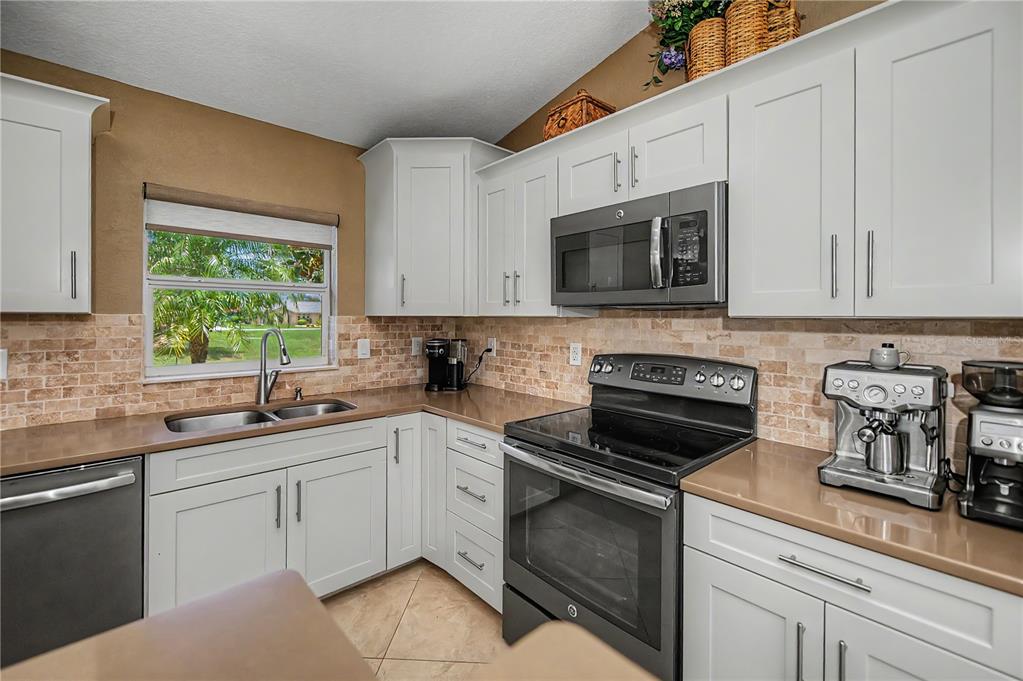 A kitchen features white cabinets, brown countertops, a tile backsplash, and stainless steel appliances — 419 BAHIA GRANDE AVENUE, PUNTA GORDA, FL