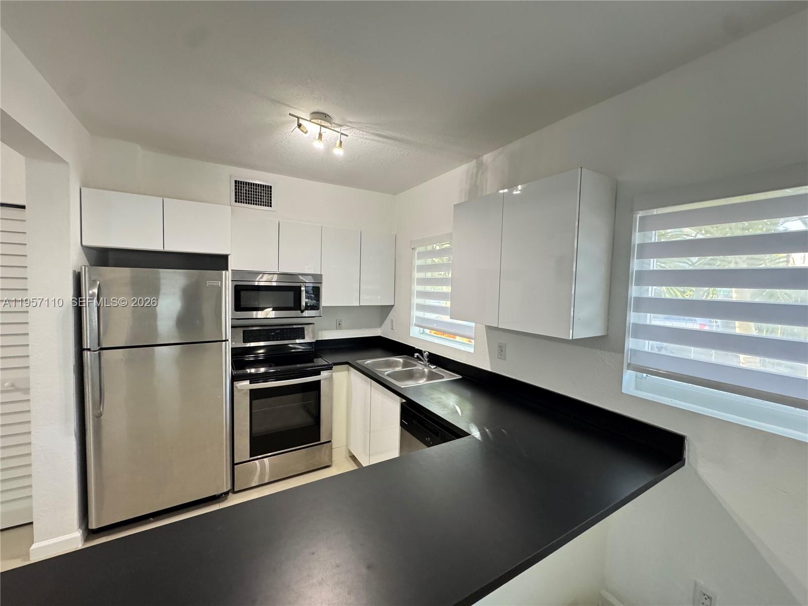 A kitchen features white flat-panel cabinets, stainless steel appliances, and black countertops — 8035 Crespi Blvd # 1, Miami Beach FL 33141, MIAMI BEACH, FL