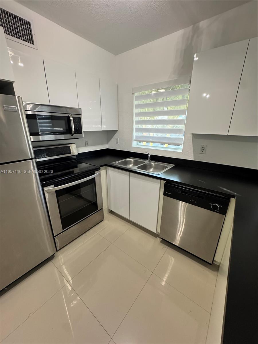 A modern kitchen features white cabinets, black countertops, and stainless steel appliances — 8035 Crespi Blvd # 1, Miami Beach FL 33141, MIAMI BEACH, FL