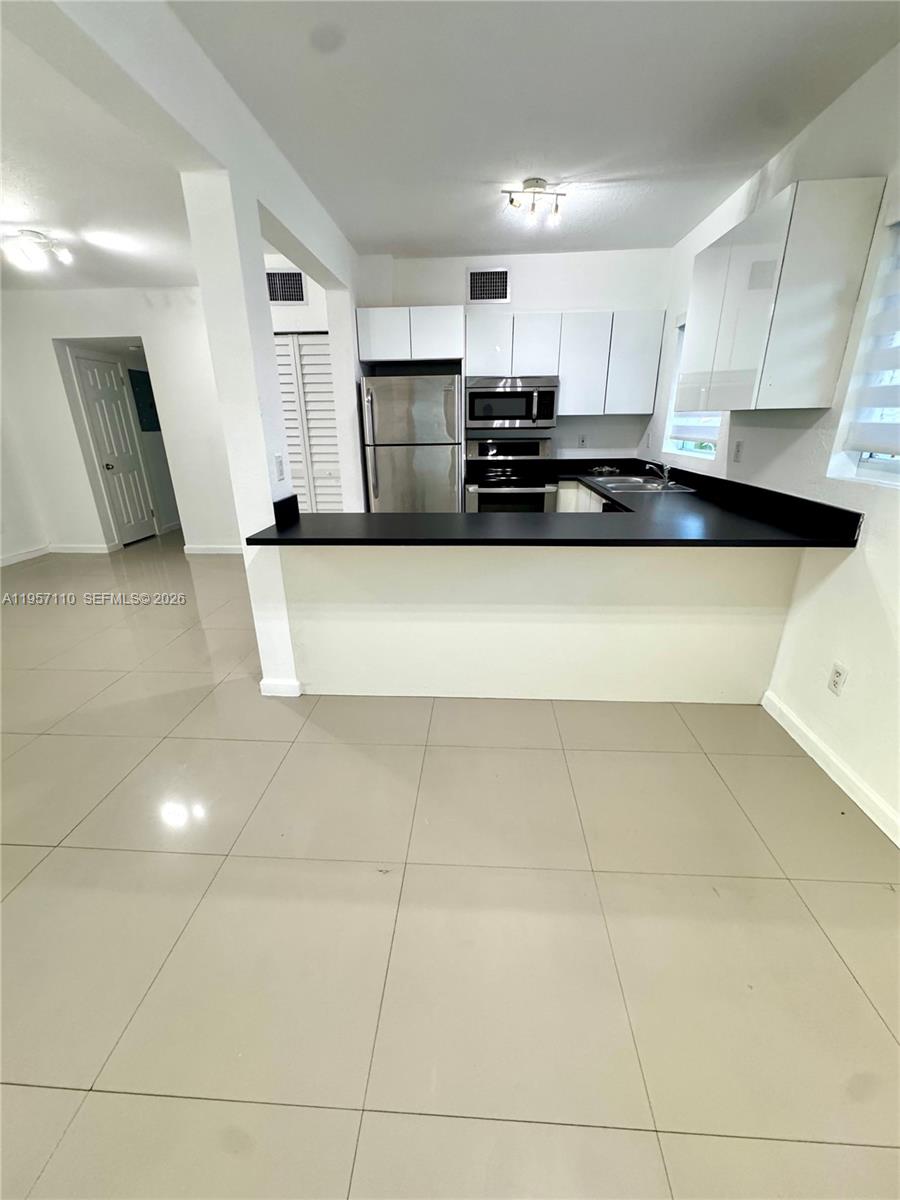 A kitchen features white cabinets, stainless steel appliances, and a black countertop peninsula — 8035 Crespi Blvd # 1, Miami Beach FL 33141, MIAMI BEACH, FL