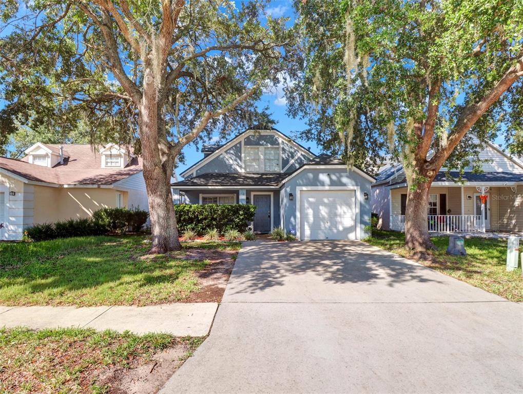 A blue house with a garage and a concrete driveway sits under large oak trees — 22817 SAINT THOMAS CIRCLE, LUTZ, FL