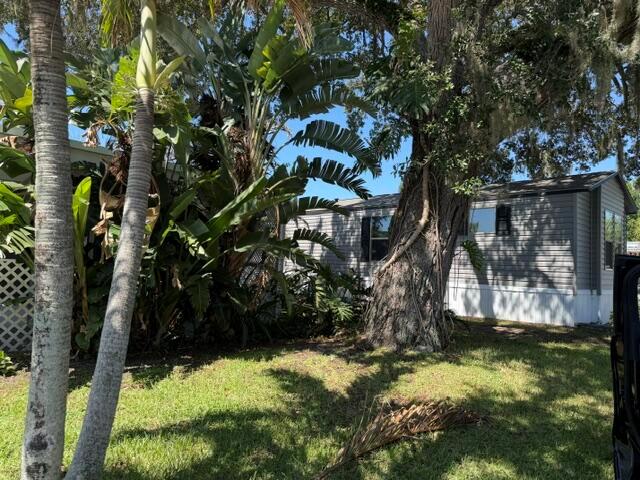 A manufactured home sits behind a large tree and lush tropical plants on a lawn — 126 Yuma Way, Fort Pierce FL 34946, FORT PIERCE, FL