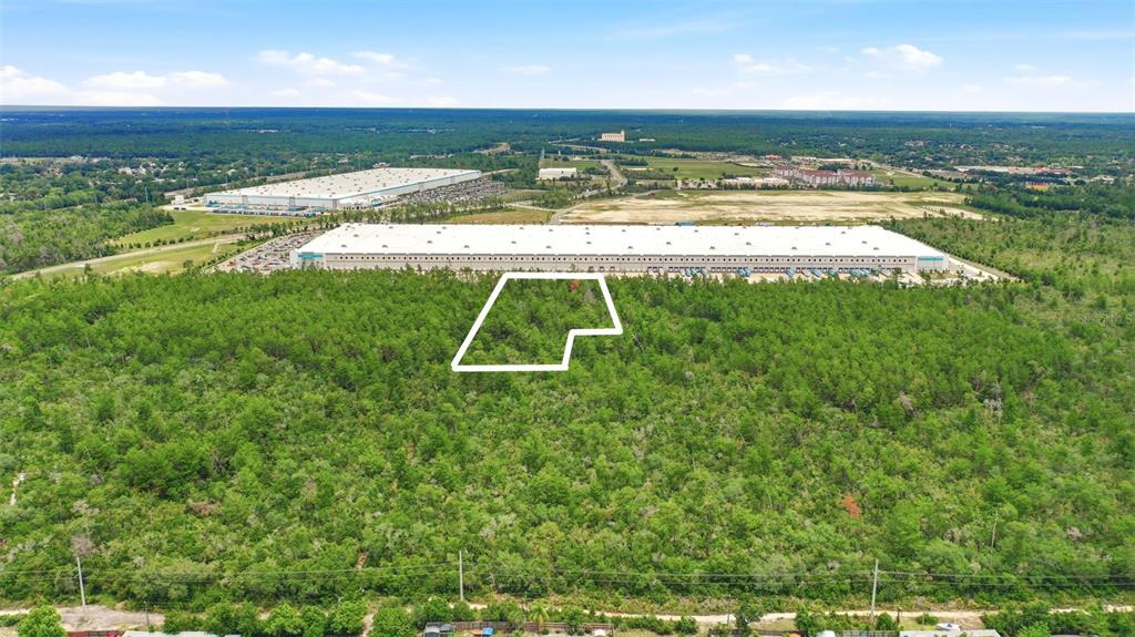 An aerial view shows a wooded lot outlined in white near a large industrial warehouse — AMELIA (PAPER) AVENUE, DELTONA, FL