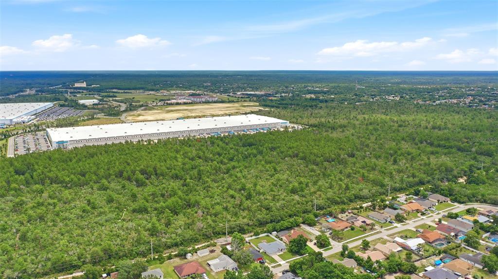 An aerial view shows a large warehouse bordering a wooded lot with a residential neighborhood — AMELIA (PAPER) AVENUE, DELTONA, FL